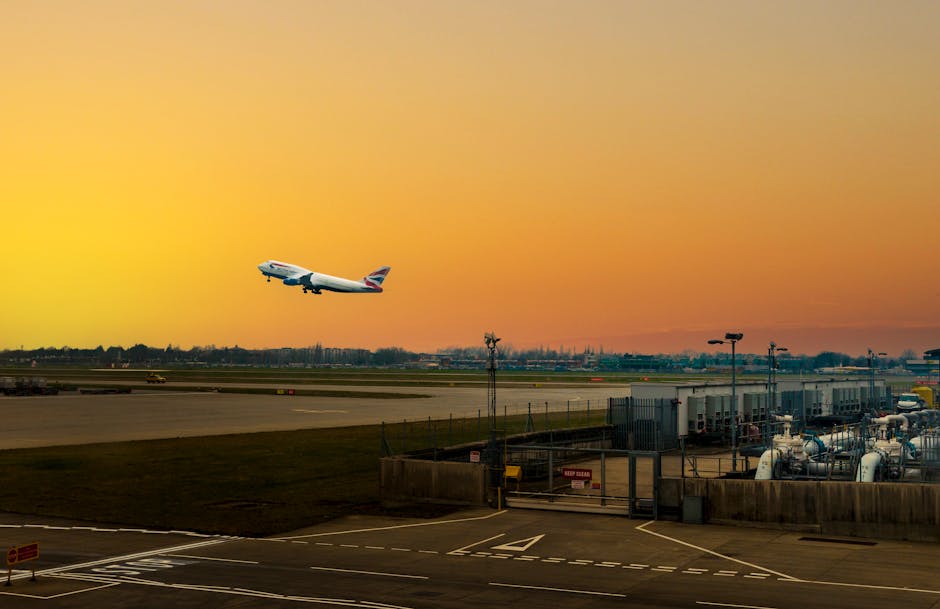 A British Airways airplane is taking off from Heathrow Airport during a vibrant sunset, with the aircraft ascending into the colorful sky. The foreground features the airport tarmac, including fuel ta