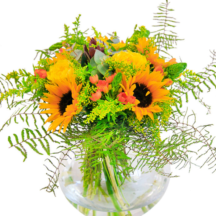 The first impression offered by this stunning Hillingdon bouquet is one of luminous celebration. A collection of radiant sunflowers and golden yellow roses beams outward, their petals layered densely and capturing the essence of late summer afternoons in neighborhoods like Hayes or near the banks of the River Pinn. Scattered throughout, glossy red Hypericum berries stand out in delightful contrast, their rich color echoing the vibrant local markets and gardens. The arrangement is rich with lush greenery: feathery fern fronds sweep gracefully, mimicking the gentle motion of the wind through local parks, while delicate yellow solidago and slender green spikes add layers of texture and color. Here and there, blue-green eucalyptus leaves peek through, introducing a touch of rustic charm and a refreshing lift. The flowers and foliage are thoughtfully arranged in a clear, round glass vase which allows the submerged stems to be on full display-adding visual interest and a sense of freshness. The bouquet radiates a gentle perfume, reminiscent of open Hillingdon fields and sun-warmed petals. Whether intended as a thoughtful gesture, a cheerful centrepiece, or a celebration for occasions like birthdays or anniversaries, this sophisticated arrangement reflects both the beauty of seasonal blooms and the welcoming nature of the local community.
