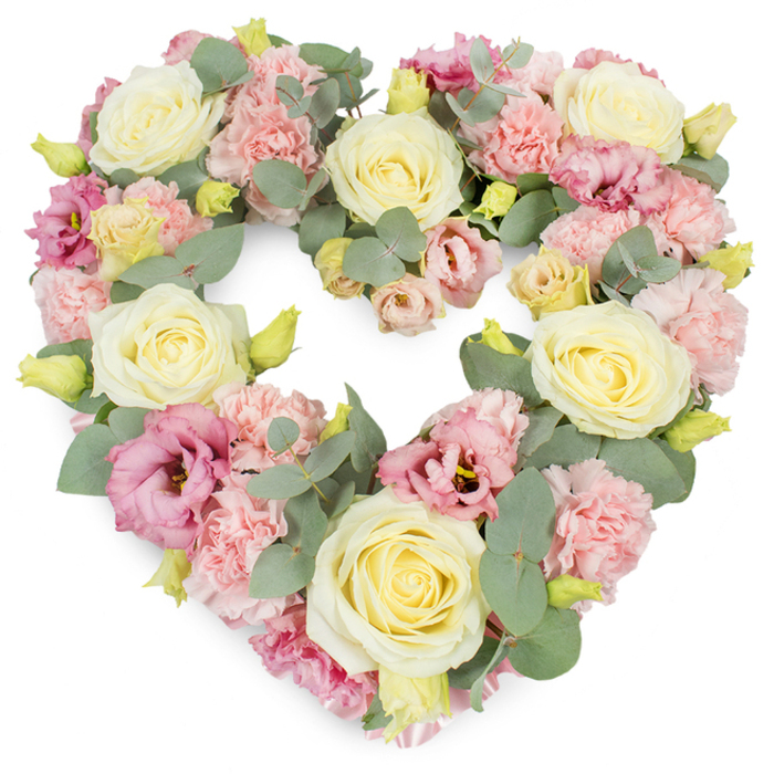 A large, heart-shaped wreath of pastel funeral flowers is set crisply against a white background, the entire form carefully packed with blossoms so that the heart feels tangible and solid, yet soft and comforting. At its core, fully open cream and pale yellow roses act as luminous focal points, their tightly layered petals forming intricate spirals that suggest tenderness and devotion. These roses are spaced to guide the eye naturally around the heart, much like following familiar routes through Hillingdon's quiet residential streets. Filling the spaces between, light pink carnations with delicately frilled petals create a plush, cloudlike texture, softening the structure and enhancing the romantic, nostalgic mood of the piece. Deeper rose-pink to mauve lisianthus blooms are tucked in throughout, their more relaxed, paper-thin petals and occasionally darker centres lending contrast and a subtle touch of drama. Cool-toned, silvery eucalyptus leaves weave throughout the flowers, their rounded, slightly matte surfaces introducing both depth and calm, reminiscent of the gentle greenery found in local Hillingdon parks. Tiny yellow-green buds punctuate the design, lifting the pastel palette with hints of new growth and quiet vibrancy. The blooms are arranged so closely that the heart seems almost cushioned, conveying a sense of being held and cherished. This wreath speaks strongly of sympathy and remembrance, ideal for honouring a loved one at a funeral or memorial service in Hillingdon. It reflects the work of a skilled local florist who understands how colour, form, and fragrance can together create a comforting presence during moments of farewell.