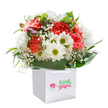 Gathered in a pristine white gift bag and nestled amongst lush, shining leaves, this jubilant bouquet captures the easy cheer of a Hillingdon spring. Envision clusters of soft coral and vivid red carnations, each petal ruffled with generous texture, close beside luminous white daisies with chartreuse-yellow centers-flowers whose crisp brightness lifts the eye just as the morning sun wakes up the fields near Ickenham Green. Baby's breath, airy as floating clouds, scatters gentle lightness throughout the ensemble, while a few purple-tinged buds add playful promise amid the established blooms. The glossy deep green foliage unfurls at the base in an elegant, natural collar, providing contrast and support as surely as the leafy lanes lining Hillingdon's historic villages. Set against a snow-white background, every element pops with clarity, highlighting the expert composition and freshly picked essence. The white ribbon handles at the top are an invitation: perfect for birthdays in Uxbridge, anniversaries in Harmondsworth, or a spontaneous gesture to brighten an ordinary day in the neighborhood. The graceful logo and script branding on the front reinforce a sense of premium care and local pride, conveying not just a bouquet but a thoughtfully arranged piece of Hillingdon to be shared and cherished.